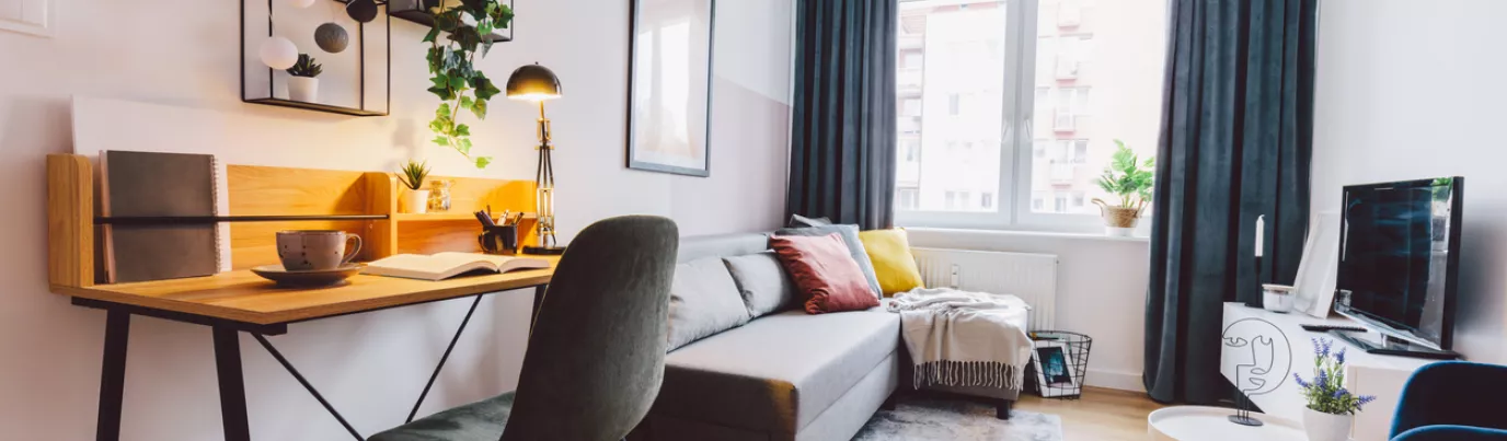 Salon moderne avec canapé convertible, bureau en bois, et étagères décorées, optimisant l'espace dans un petit appartement.